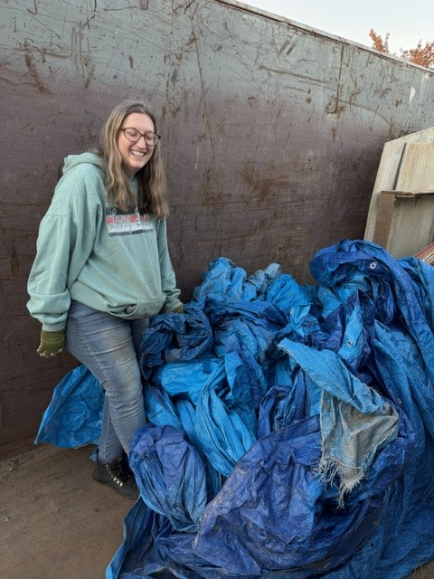 Volunteer standing beside a container filled with blue tarps