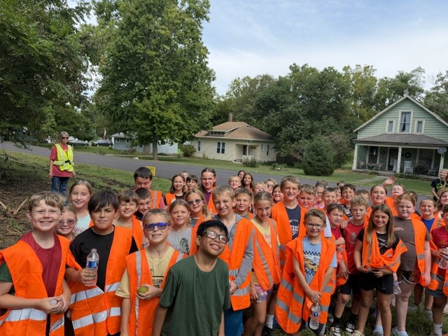 Group of children in orange safety vests gathered outdoors after a cleanup